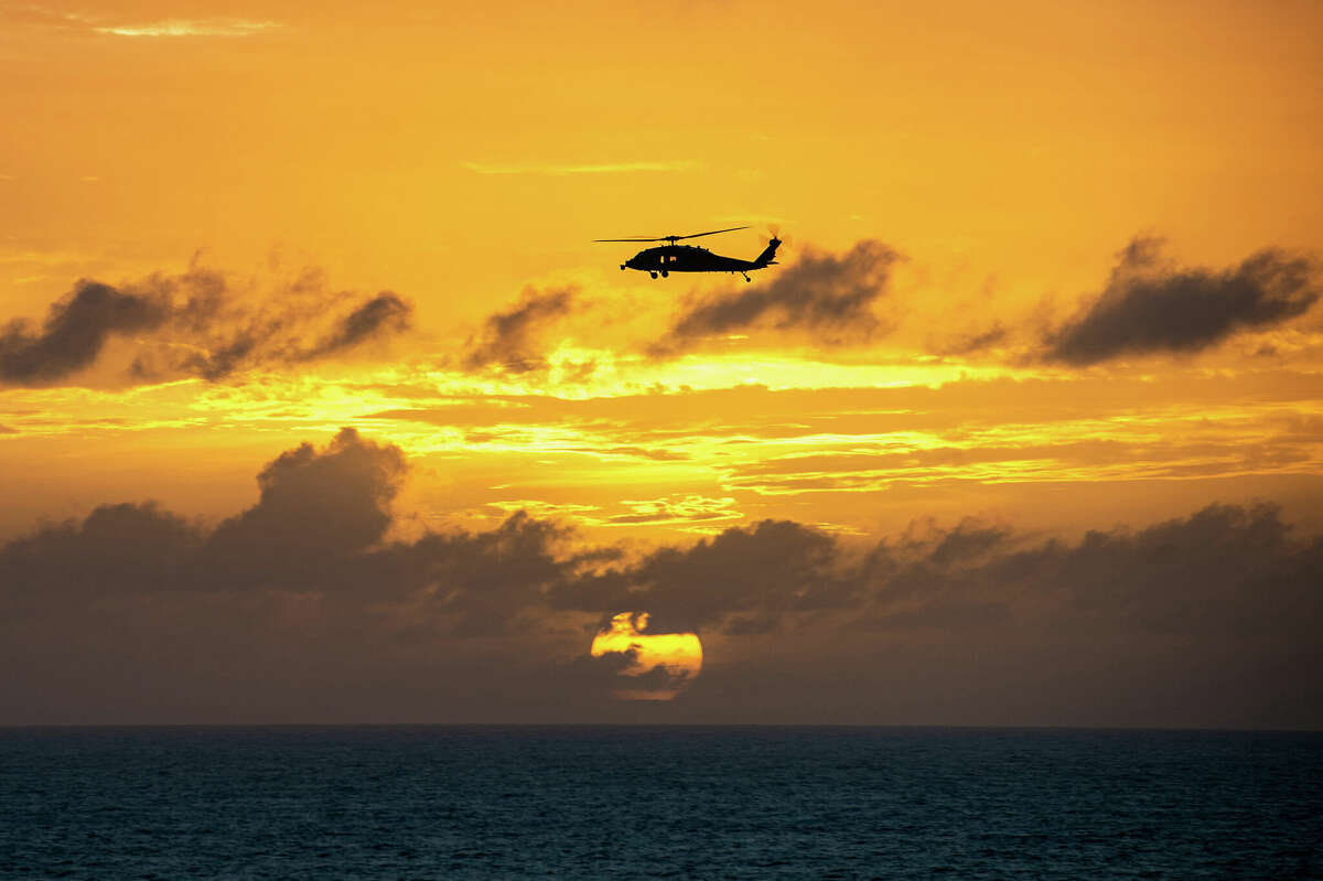 Against a setting sun, a Sikorsky MH-60S Seahawk helicopter attached to Helicopter Sea Combat Squadron 6 flies in December 2022 near the aircraft carrier USS Nimitz in the Pacific Ocean. 