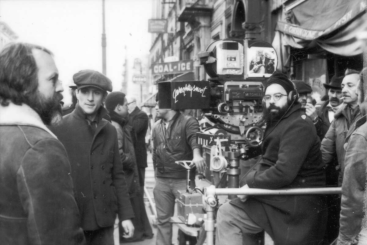 American director Francis Ford Coppola sitting with the camera on the set of his film "The Godfather Part II." Robert De Niro is standing at left.