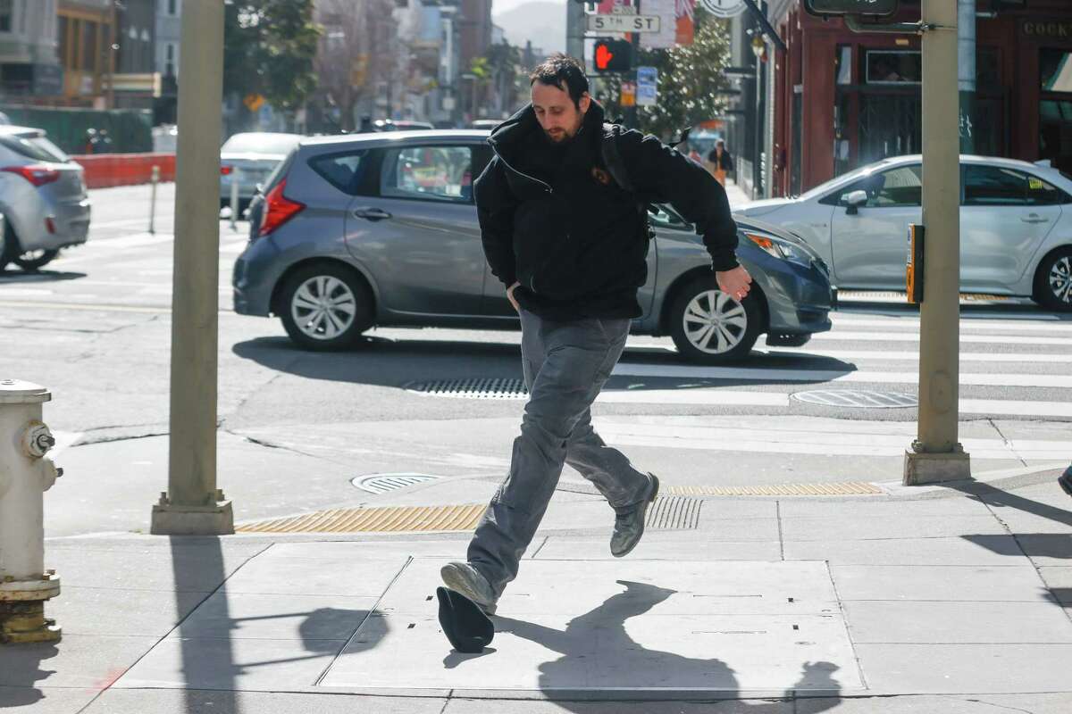 2023年2月21日，星期二，加州旧金山，Pacifica的尼克·卡塔拉诺在走在第五大街上时，在强风中把帽子弄丢了，他正在追赶帽子。