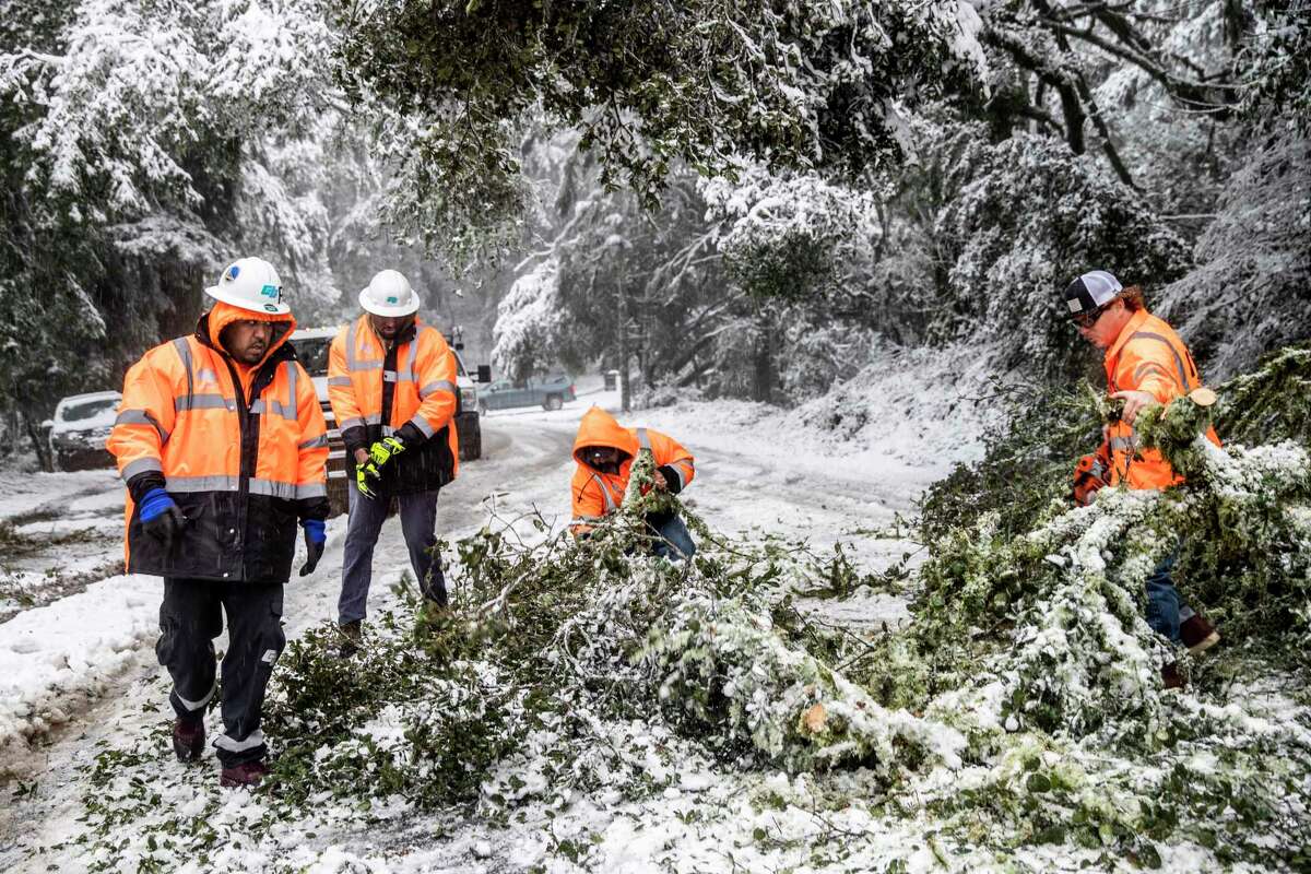 Caltrans workers remove a downed tree along snow-laden Skyline Boulevard in Woodside.