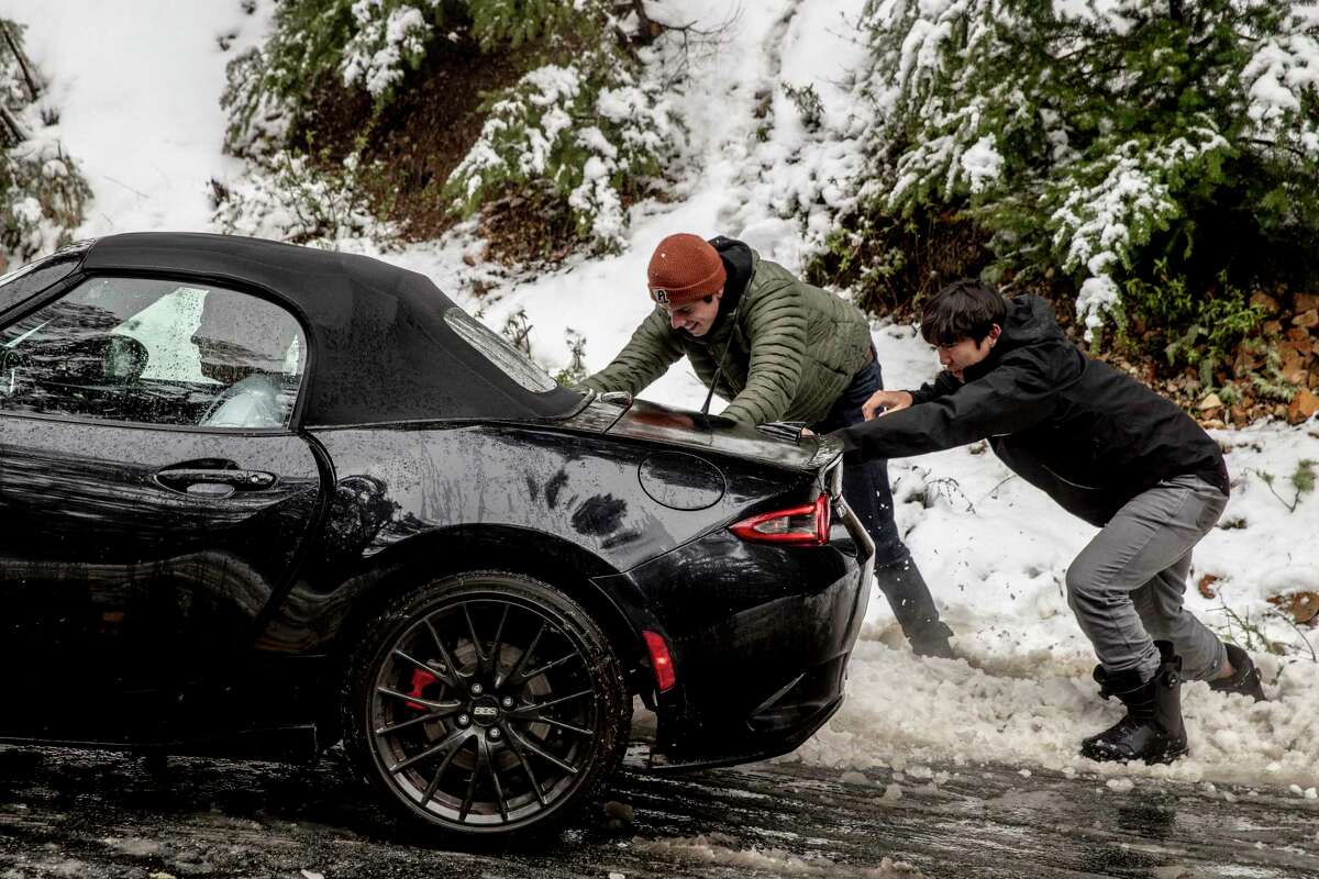 Jason Wu (right) and friend Dmitriy Luck push motorist John McLeod’s vehicle after it became stranded because of snow and ice along Skyline Boulevard in Woodside.