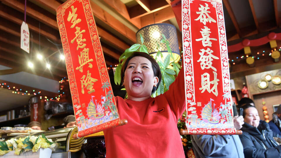 Restaurant owner Rain Wang holds up scrolls wishing good luck and a happy New Year during the dragon dance performance at Sushi Soba in Old Greenwich, Conn. Sunday, Feb. 26, 2023. After a two year hiatus, the dragon dance returned to Sushi Soba on Sunday to bring good luck for Chinese New Year. The restaurant celebrated its eight year anniversary and the opening of a new restaurant on Greenwich Avenue, Poke Boba.