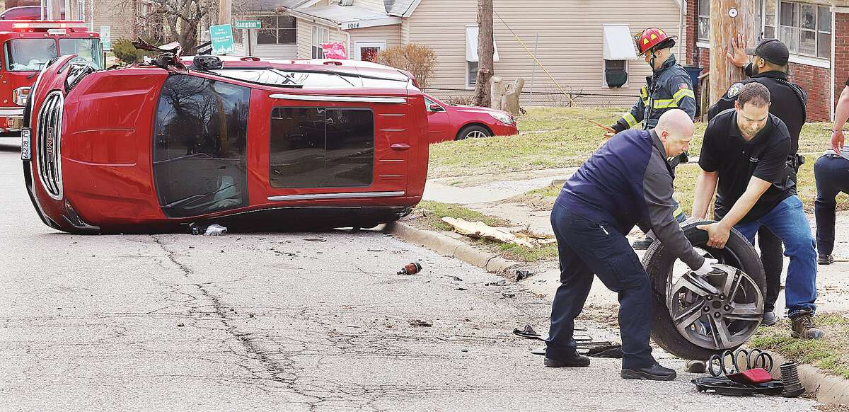 A passerby, right, helps an Alton firefighter remove the wheel of a GMC Terrain from the 1100 block of Brown Street in Alton Sunday afternoon. 