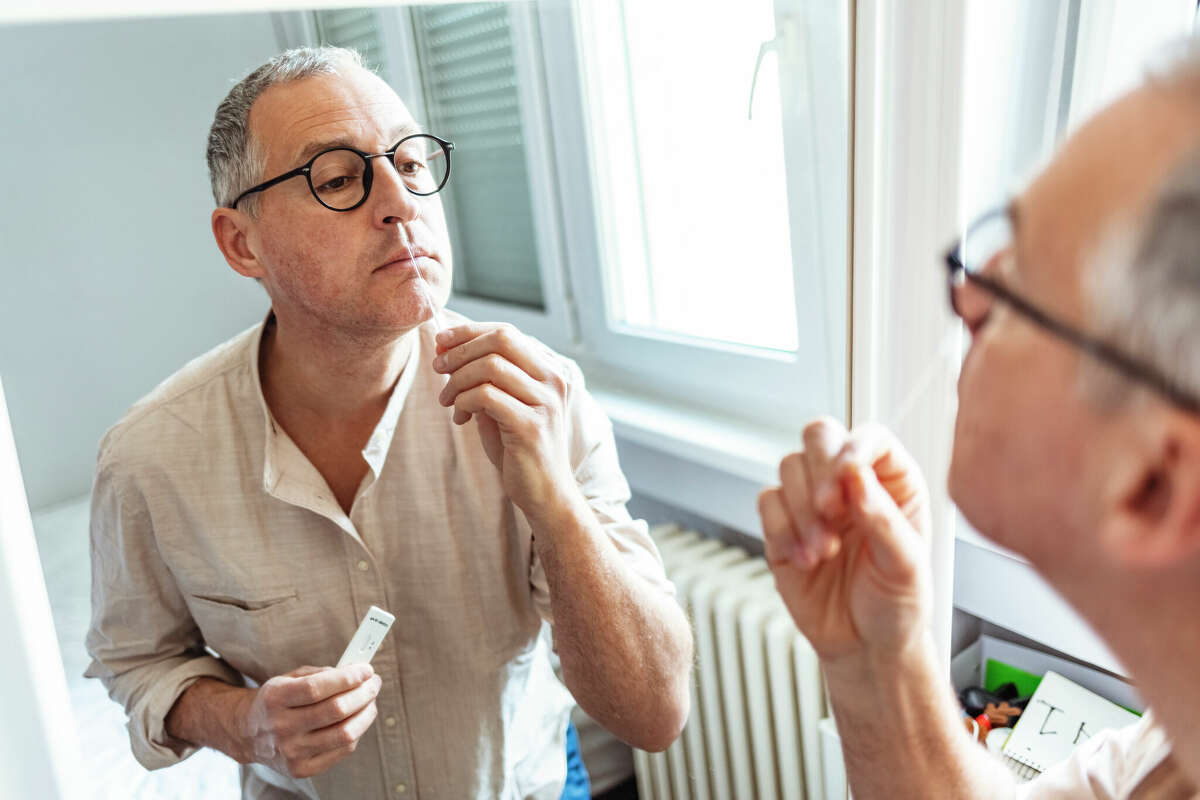 STOCK PHOTO: Mature man doing self test for COVID-19 at home with Antigen test kit. Coronavirus nasal swab test for infection.