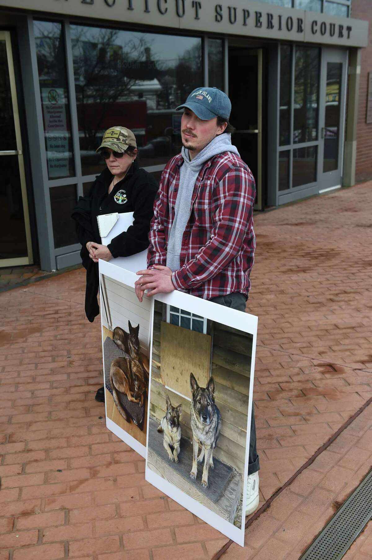 Shane Caviola with photographs of his family’s dogs Cimo, right, and Lieben, left, on a poster outside Danbury Superior Court on Wednesday. Michael Konschak has been charged in connection with the deaths of her two dogs.