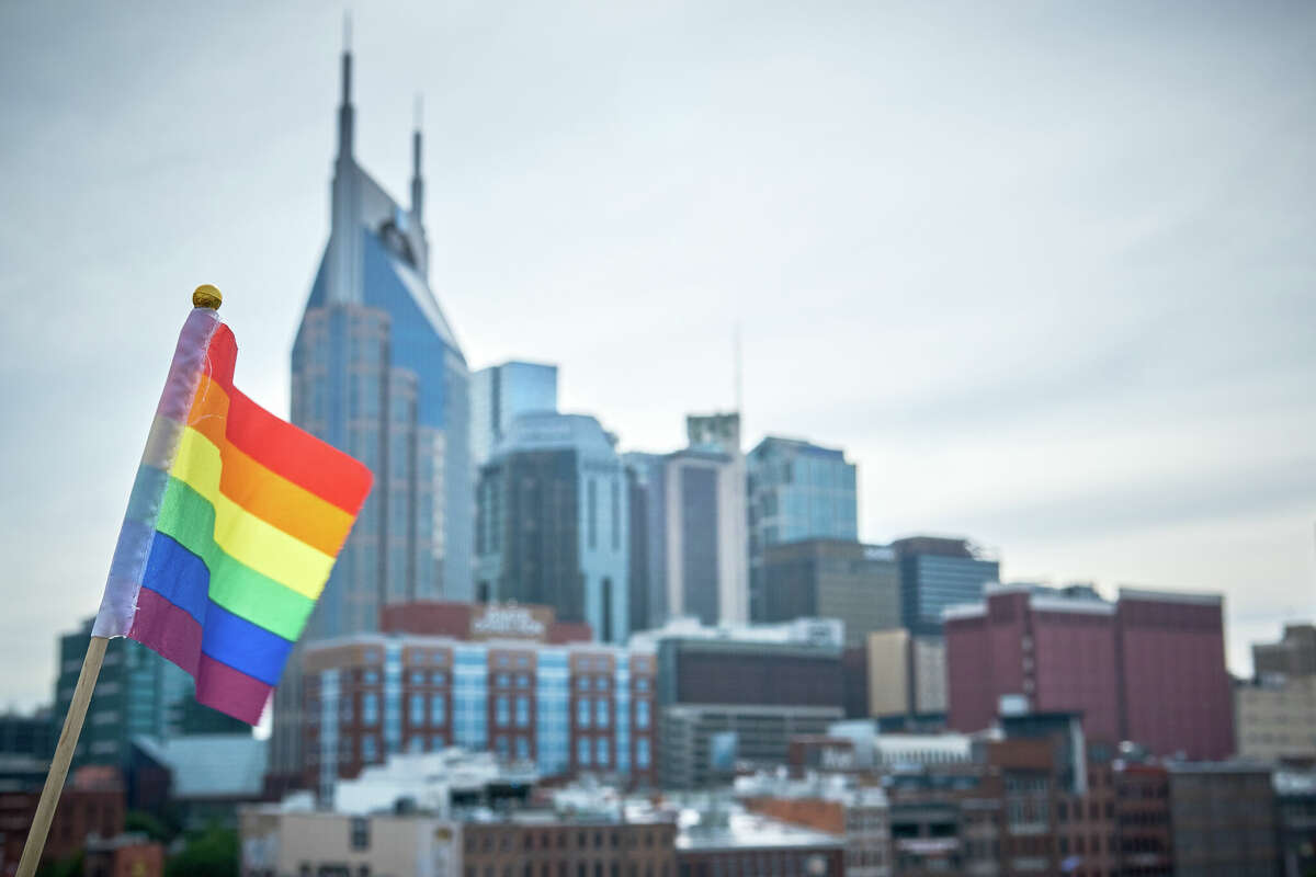 Rainbow flag in the foreground with the city skyline of Nashville, Tennessee in the back on an overcast day.