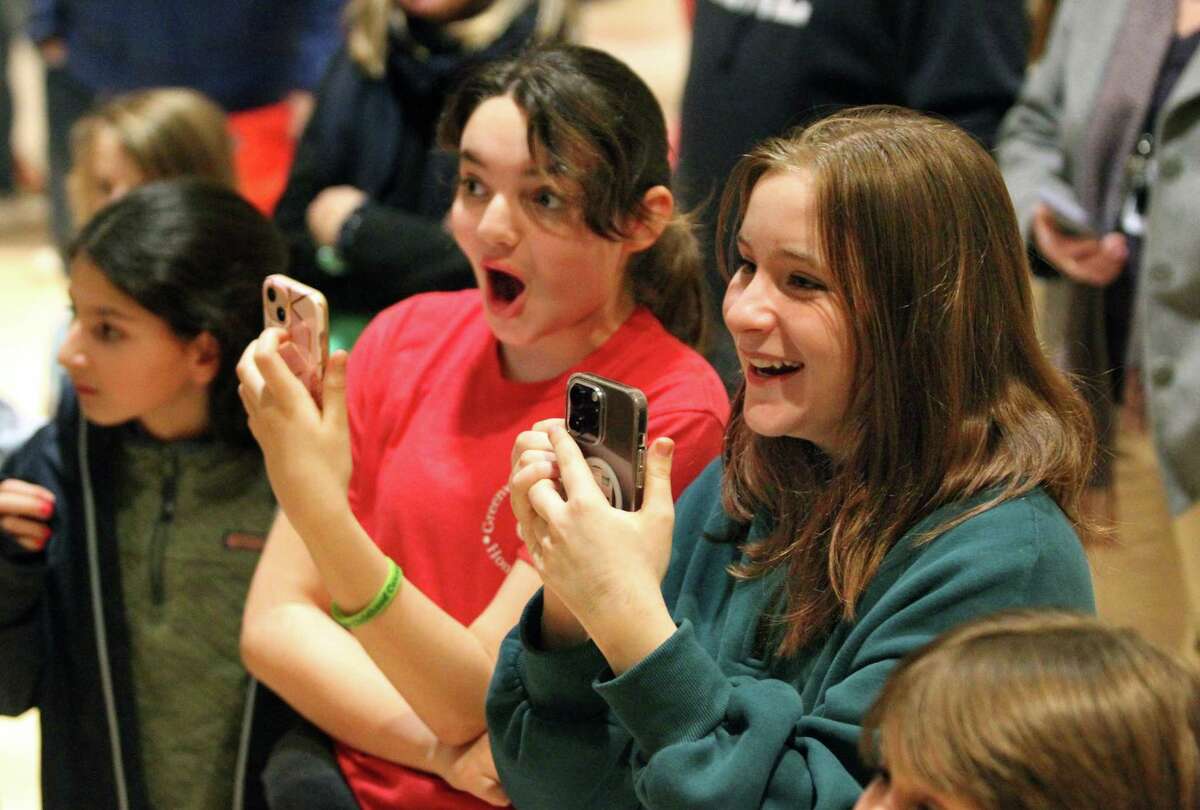 Students Jennifer Pereira, center, and Natasha Achoa, right, watch and react as classmate Oliver Sanders has his hair removed during a head shaving/hair donating event to raise awareness and money for childhood cancer research and the St. Baldrick's Foundation at Cos Cob Elementary School in Greenwich, Conn., on Thursday March 2, 2023. This volunteer-driven event was held in an attempt to show solidarity with the children who lose their hair undergoing treatment and featured professional barbers, catering, and the live band The Sound Cats. Also, participants donated their ponytails (eight-inch minimum). The St. Baldrick's Foundation event has been an annual GPS tradition since 2013 and spearheaded by Cos Cob Principal Kerry Gavin.