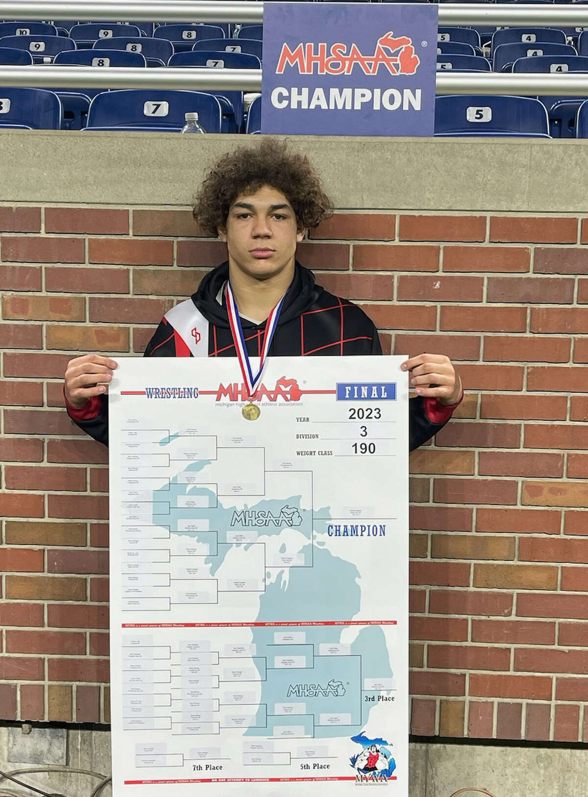 Reed City's Bryson Hughes shows his medal and the state championship bracket after finishing first on Saturday, March 4, at Ford Field/