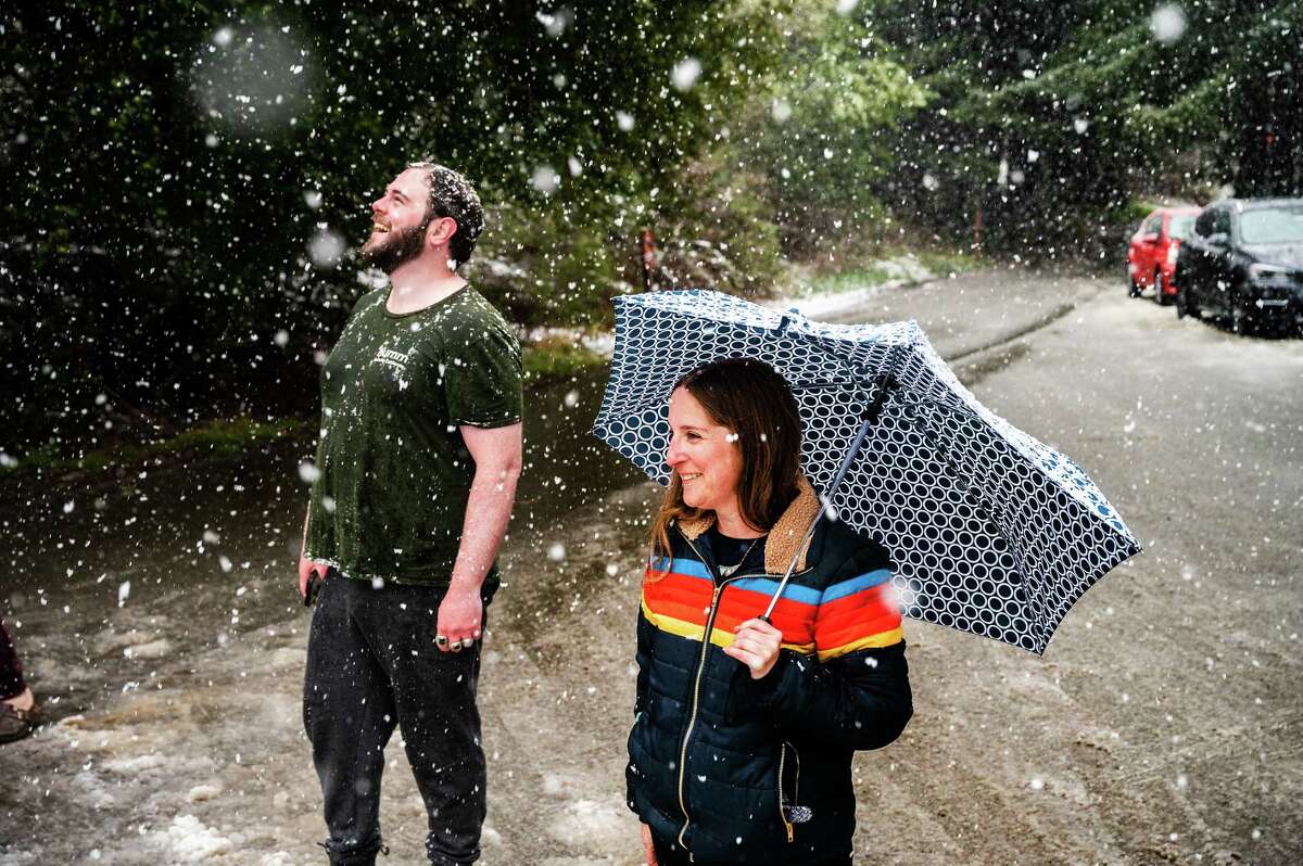 Snow falls on Angela Coppola and Iain McIntyre in Tilden Park on Friday, Feb. 24, 2023, in Berkeley, Calif. Coppla, a Berkeley High School teacher, used her lunch break to see the snow.