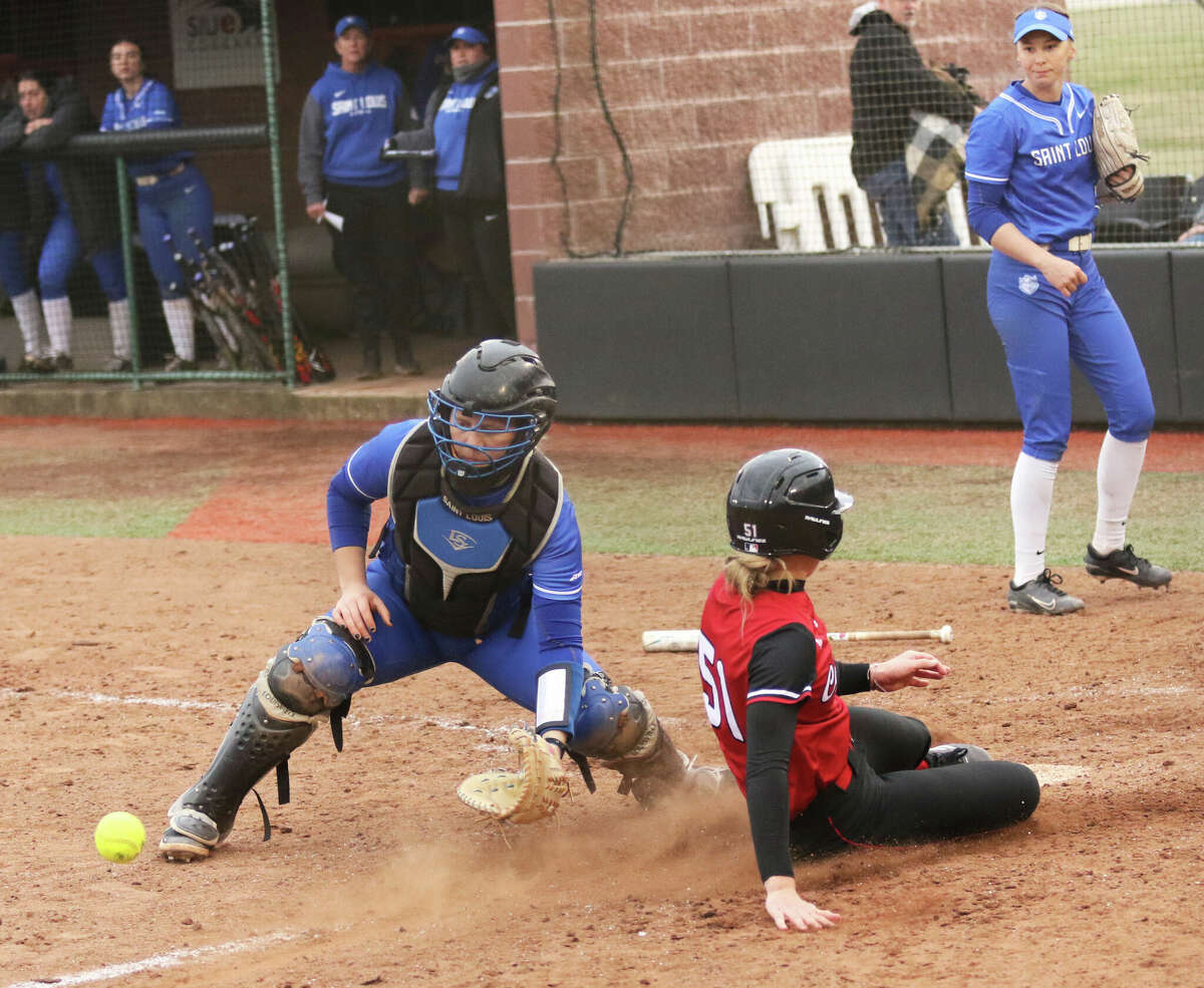 SIUE pinch runner Sam Breed (right) slides across the plate with the winning run ahead of the throw to SLU catcher Kelsey Etling (left) while Bills pitcher Chloe Wendling watches her win turn to a loss Wednesday afternoon at Cougar Field in Edwardsville.