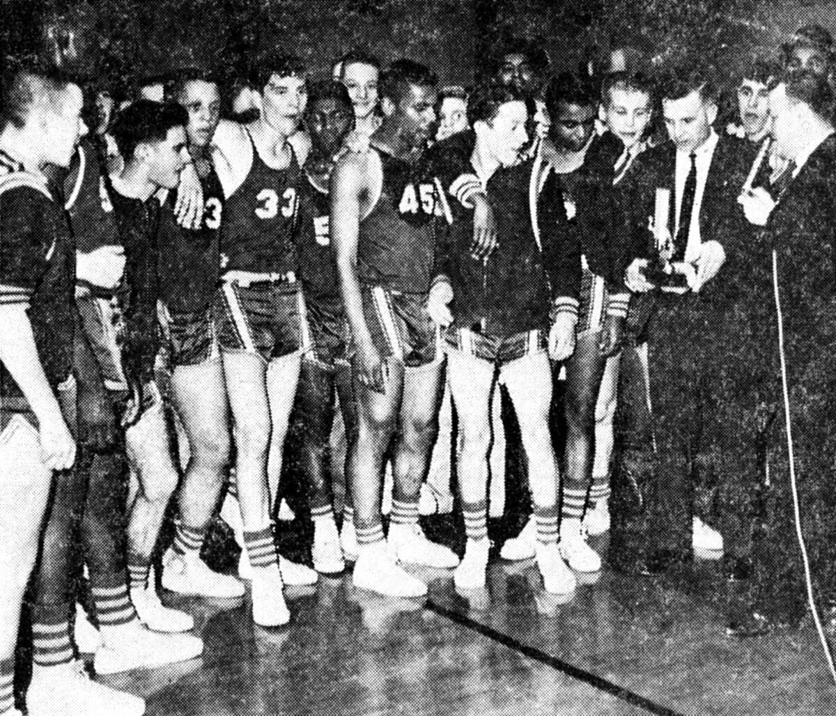 Ken Rutherford, Manistee High School basketball coach (far right), is presents the Class D district championship trophy to coach Doyle Eckhardt of the Norman-Dickson Norsemen who won the district tournament game against the Onekama Portagers Saturday night at the Armory. The photo was published in the News Advocate on March 11, 1963.