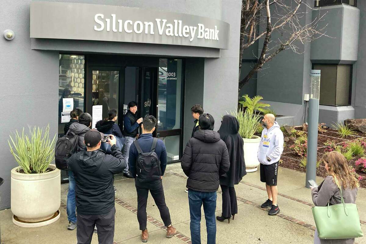 A person from inside Silicon Valley Bank, middle rear, talks to people waiting outside of an entrance to Silicon Valley Bank in Santa Clara, Calif., Friday, March 10, 2023. The Federal Deposit Insurance Corporation seized the assets of the bank on Friday, marking the largest bank failure since Washington Mutual during the height of the 2008 financial crisis.