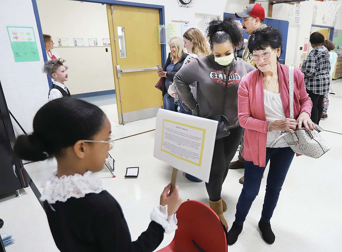 Parents and family members stop to listen to "wax figures" like Susan B. Anthony, portrayed by Zoe Phillips, foreground, and Albert Einstein played by Parker Lewis, background.
