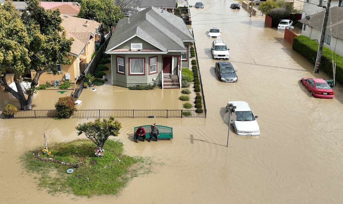 An aerial view shows people sitting on a bench in a flooded neighborhood in the unincorporated community of Pajaro in Watsonville, Calif., on Saturday.