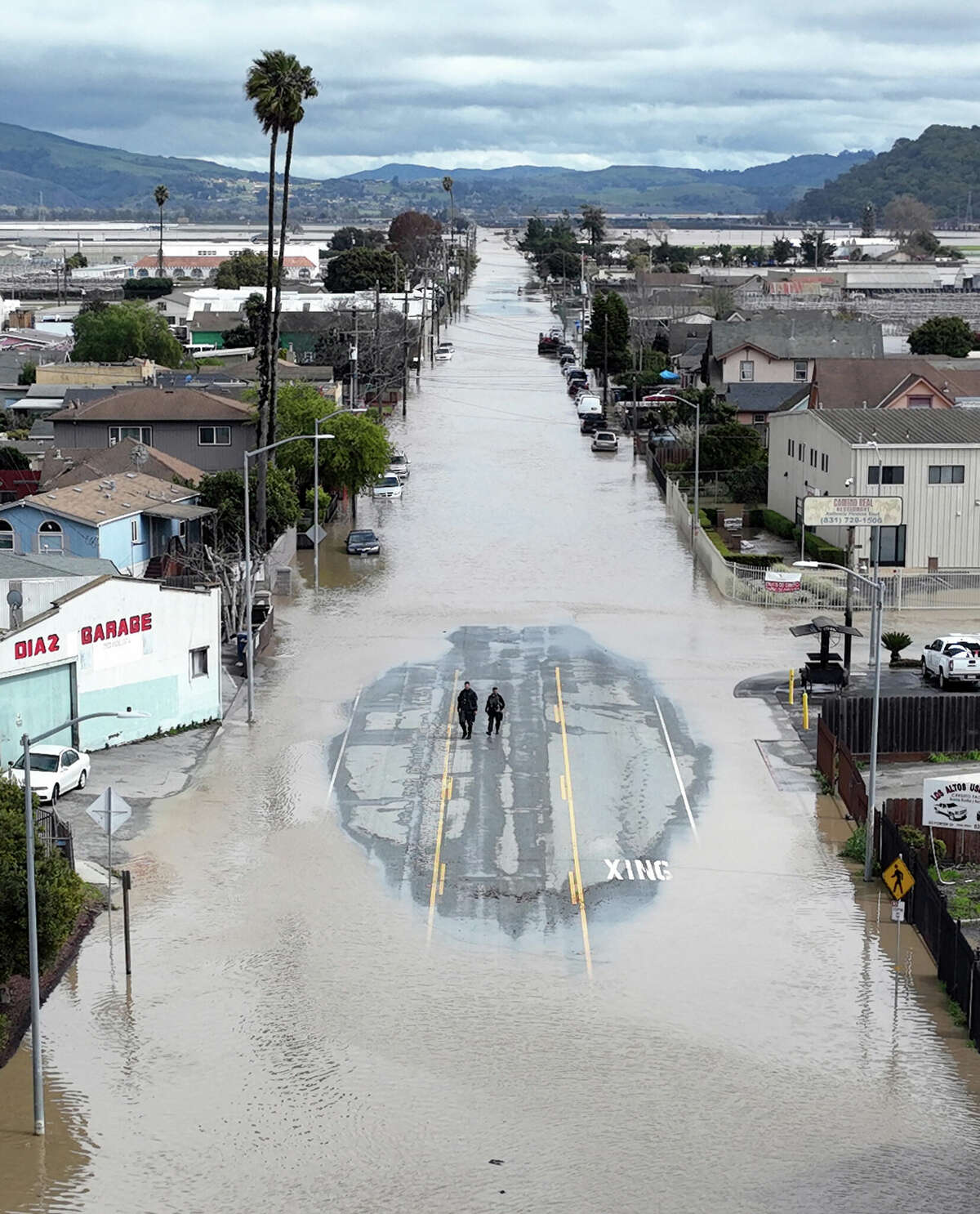 Two individuals stand in a small patch of road emerging from floodwaters in Pajaro, Calif., on Saturday.
