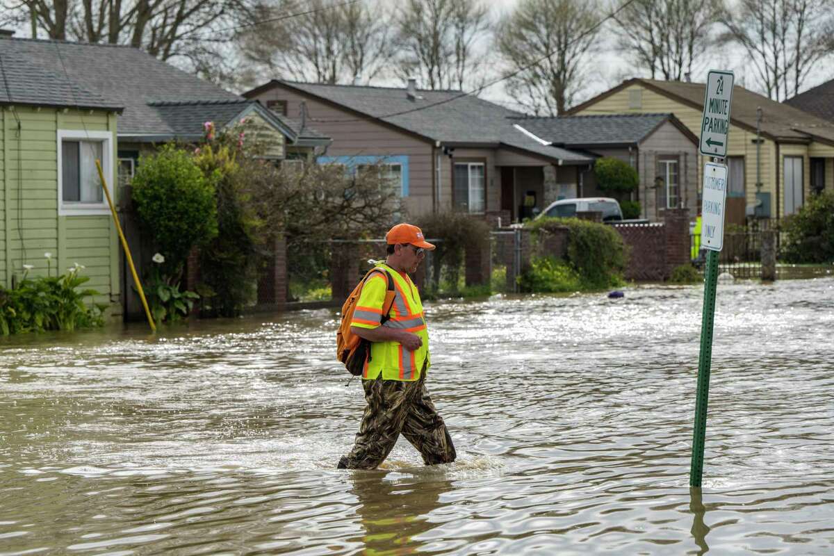 A member of the USGS geological survey team walks through a flooded street in Watsonville.