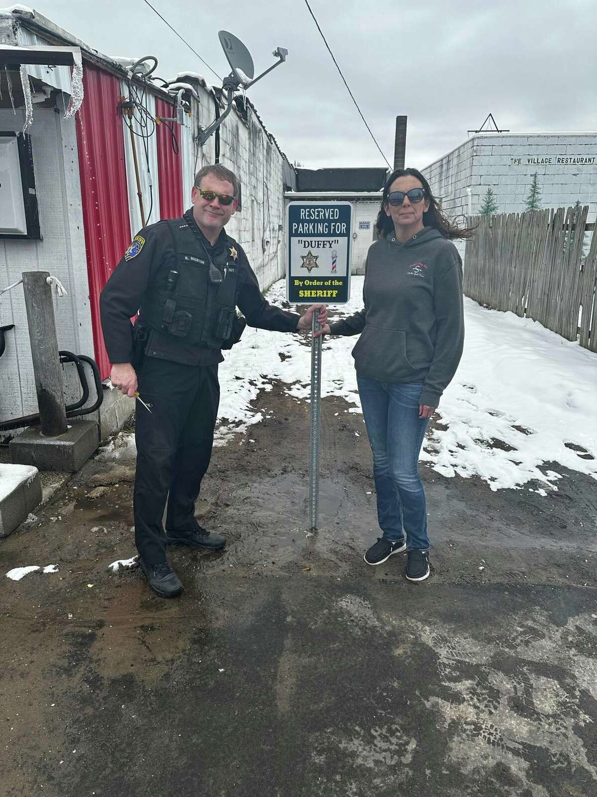 Lake County Sheriff Rich Martin (left) and Missy Boss, manager of Shoey's Log Bar, 846 Michigan Ave., install a donated parking sign for Noel "Duffy" Duffing behind his barber shop in downtown Baldwin.