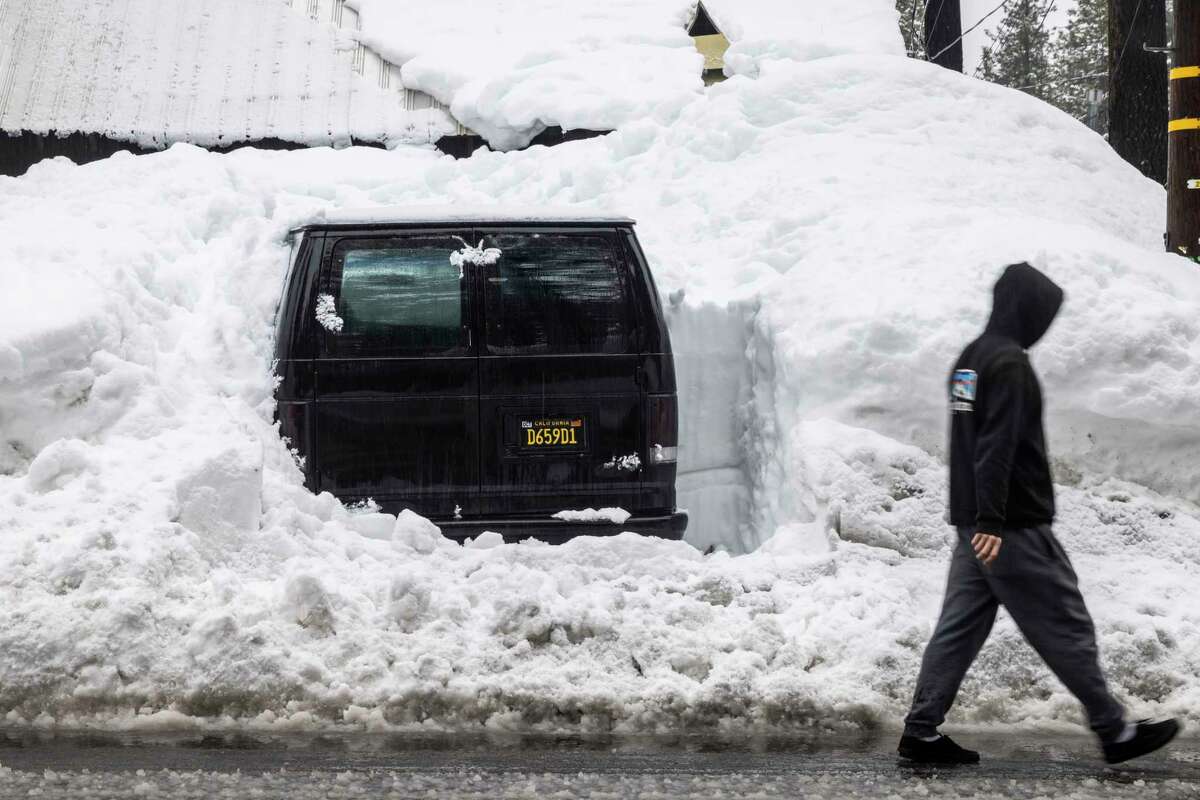 A pedestrian walks past a snowed-in vehicle near Dollar Point, Calif. Tuesday, March 14, 2023.