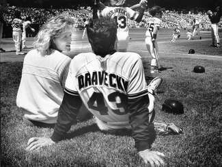 San Francisco Giants pitcher Dave Dravecky sits on the lawn with his wife Jan with his back to the camera as he watches children play softball. 