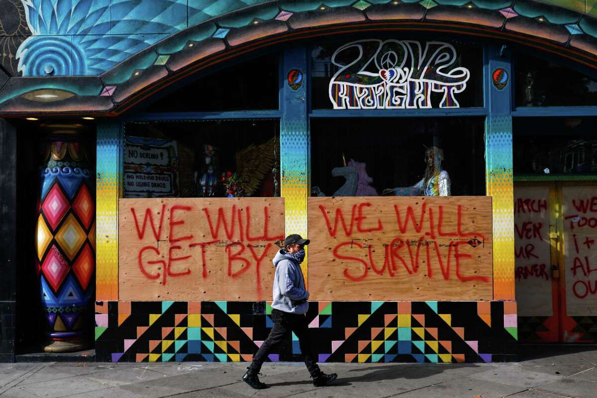 Alex Wolf passes by a store that is boarded-up and written on with supportive messaging on Haight Street in San Francisco on March 17, 2020. The city was ordered to shelter in place due to the coronavirus.