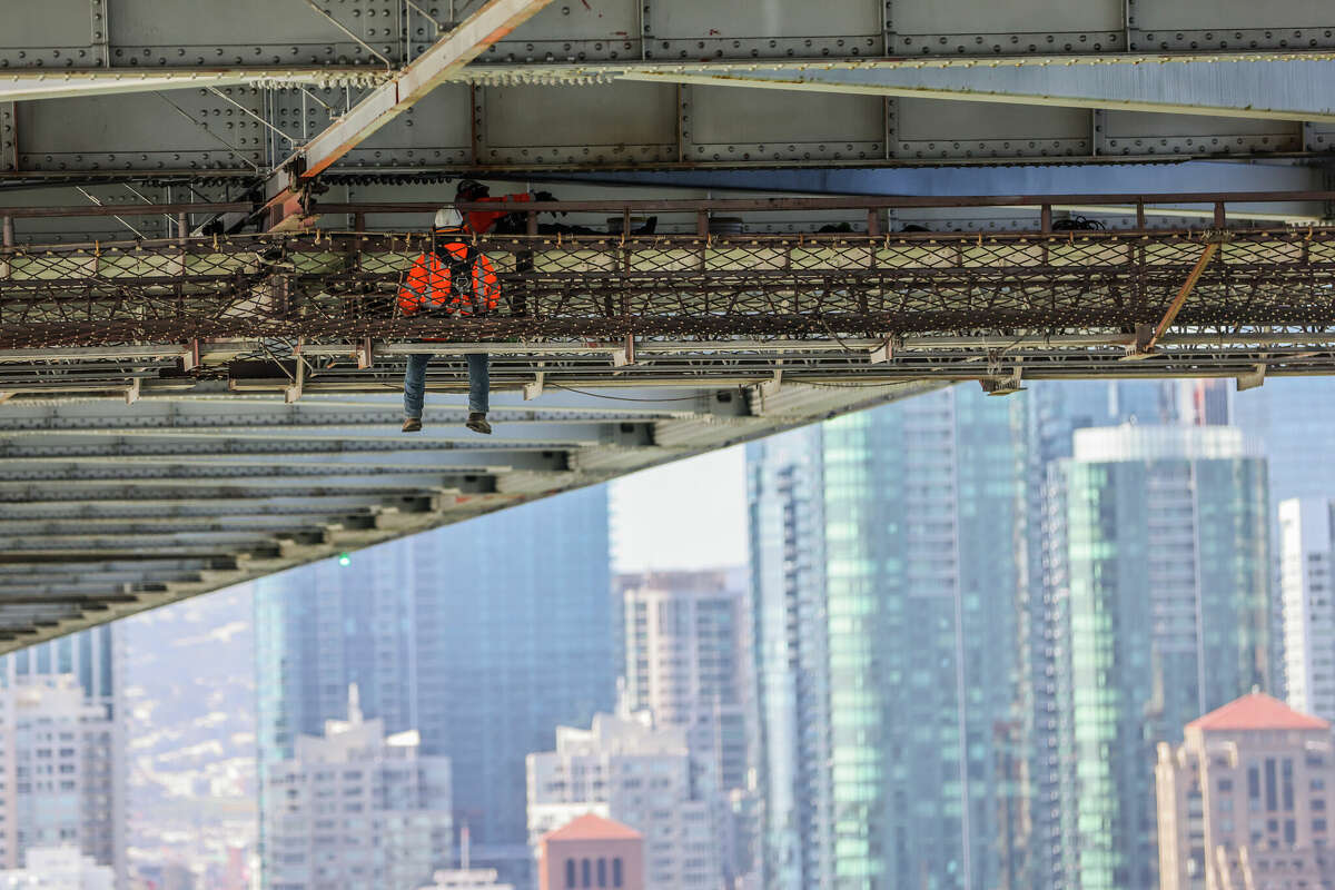 A worker dangles from the underside of the Bay Bridge as he paints on Thursday in San Francisco .