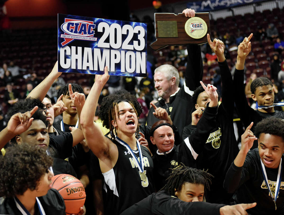 WCA's Aiden Cross (5) holds a state champions sign with his teammates after No. 2 Waterbury Career Academy's 74-58 win over No. 1 Bloomfield in the CIAC Divison III boys basketball championship at Mohegan Sun Arena in Uncasville, Conn. Sunday, March 19, 2023.