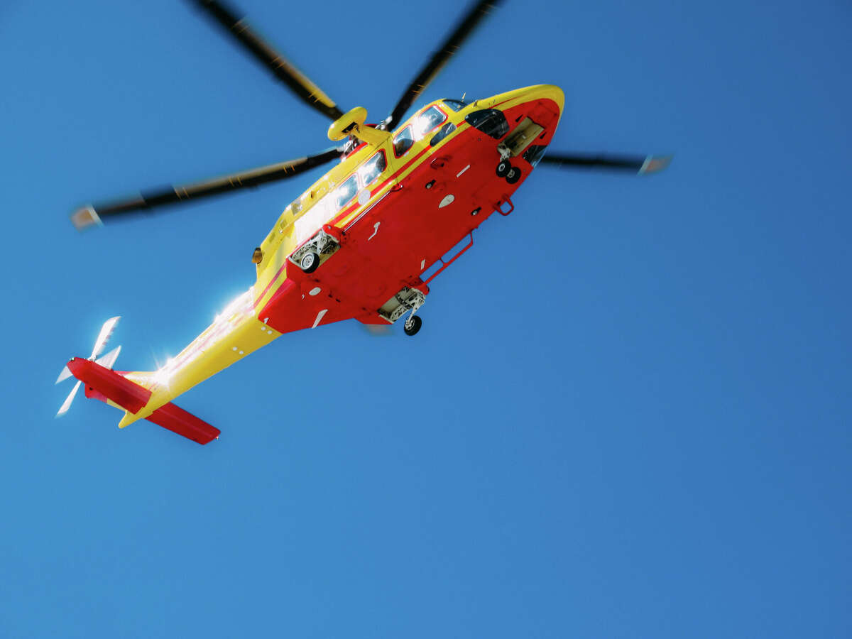 View from below of rescue helicopter in vibrant red and yellow colors. Helicopter flying overhead and sky totally clear and blue.