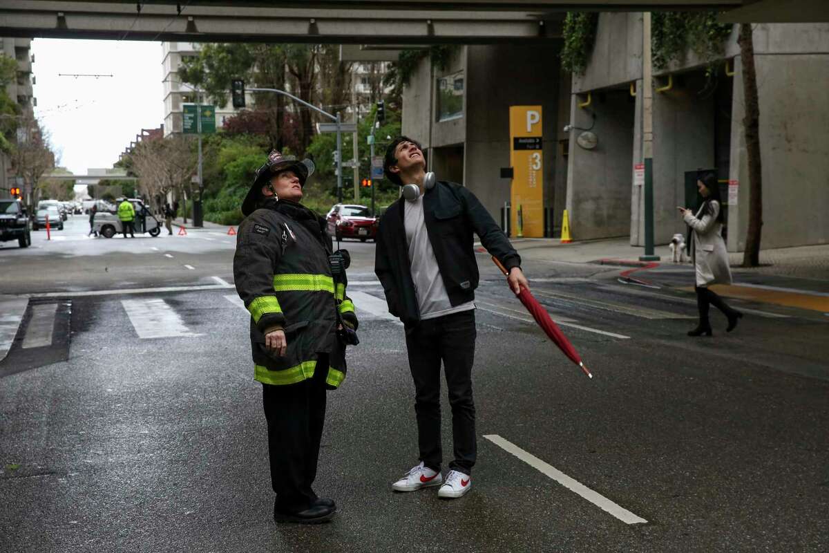 旧金山消防部门的一名成员在萨克拉门托街和戴维斯街的十字路口引导一名行人，由于加州50号大楼几层楼高的窗户破碎，该路口禁止交通。