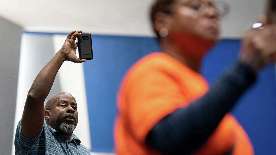 Larry McKinzie, left, films with his phone during a TEA community meeting with Alejandro Delgado, TEA Deputy Commissioner, Office of Operations. The TEA hosted the first of four community meetings where people can come ask questions and learn more about the state takeover of HISD at Westbury High School on Tuesday, March 21, 2023 in Houston.
