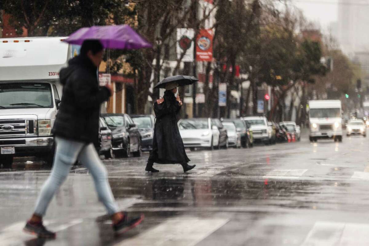 周二，在大雨中，人们打着雨伞穿过旧金山的瓦伦西亚街。
