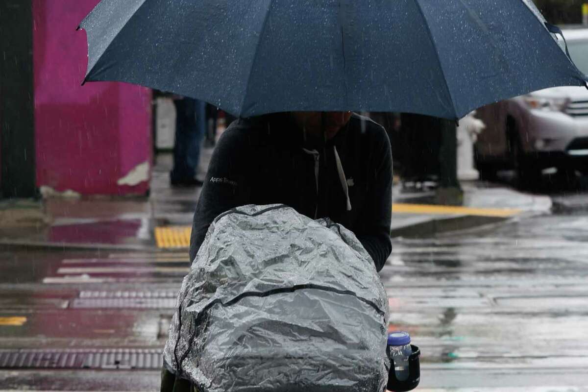 A toddler sits under the rain cover of a double stroller while being pushed by an adult with an umbrella in the rain in San Francisco, California, Wednesday, March 29, 2023.