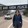 Houston artist Chandrika Metiver stands in front of the "NO WAR KNOW PEACE" message they wrote on the Union Pacific Bridge over I-45. 