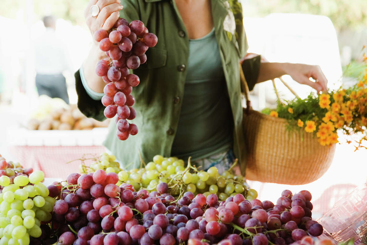 A woman picks out grapes at a farmers market stand.