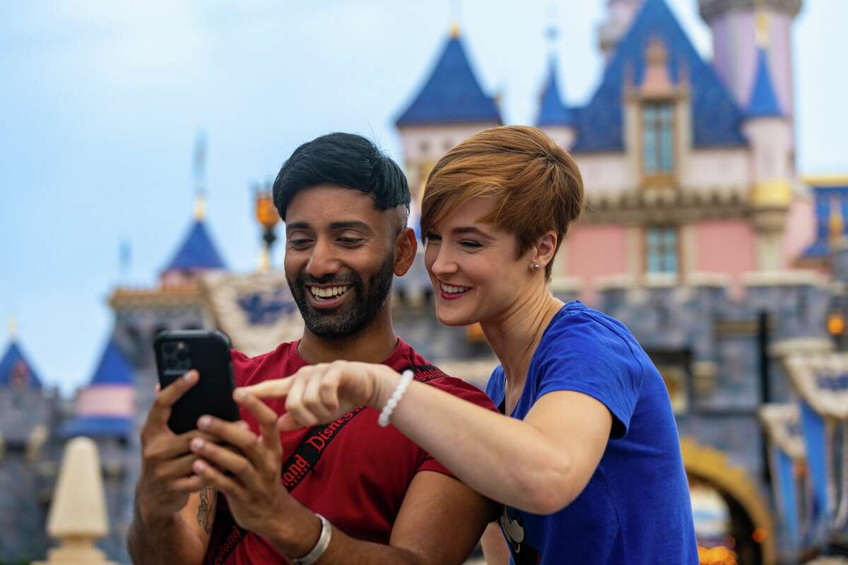 Two guests in front of Sleeping Beauty Castle at Disneyland use the resort's app to navigate the park.