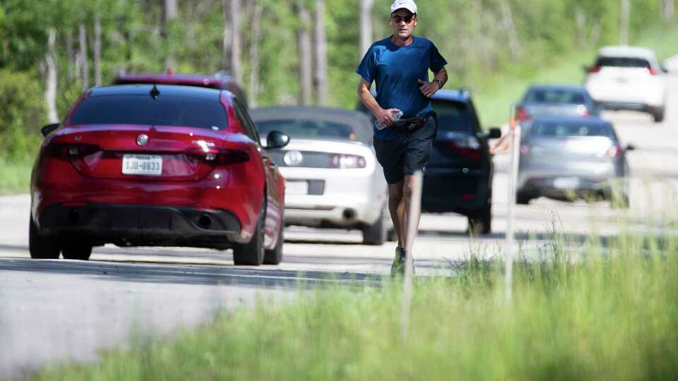 A man jogs along Kuykendahl Road as vehicles pass by, Tuesday, April 11, 2023, in The Woodlands.