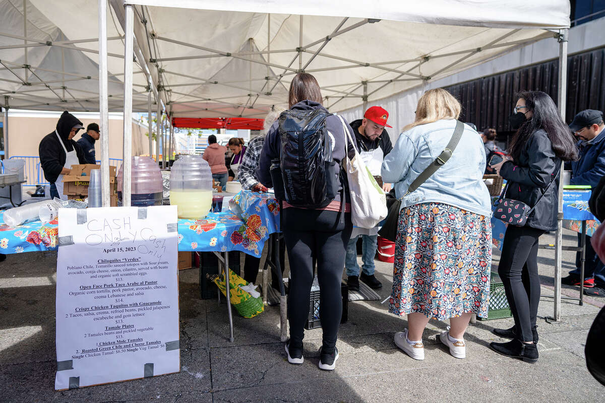 People order food next to the menu at the Primavera stall at the Ferry Plaza Farmers Market on Saturday, April 15, 2023.