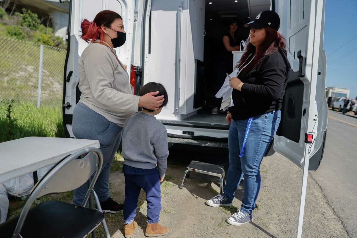 在诺瓦托外宾福德路房车营地的居民的外展和资源活动中，莉迪亚·劳达和她4岁的儿子伊曼纽尔站在一起，与马林县的社会工作者Aracely Cañas交谈。