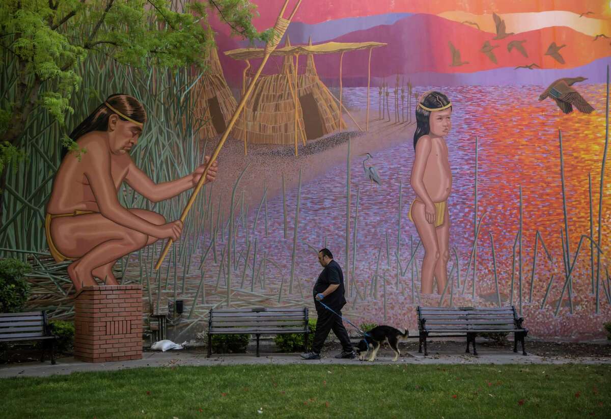 Paul Lopes walks his dog Fang near a mural depicting life along Tulare Lake for the native Tachi Yokut tribe. Many in the tribe are happy to see the return of the lake, which was their ancestral home.
