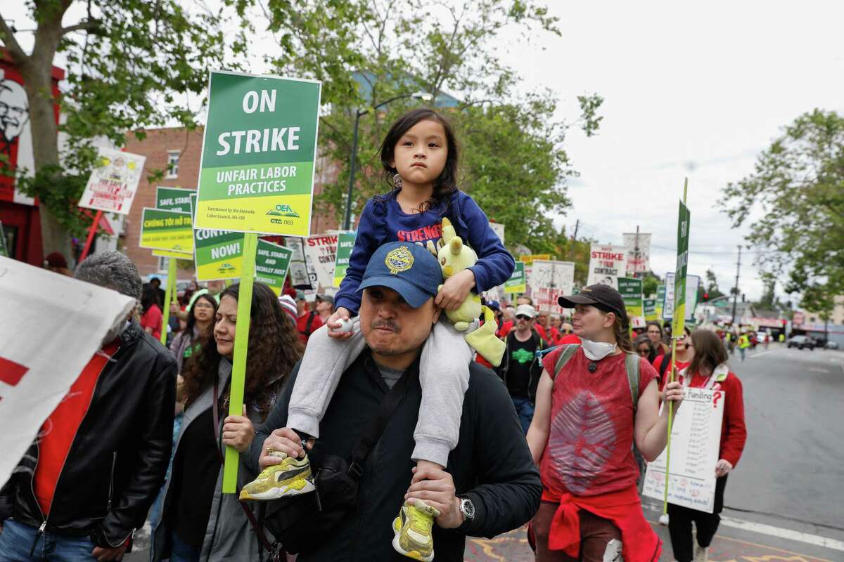 2023年5月5日星期五，奥克兰教师罢工期间，一名奥克兰学生的父母和一名教师的丈夫欧文·马(Owen Ma)和他5岁的女儿奥尼克斯·马(Onyx Ma)在他的肩膀上游行，与其他支持者和OEA成员一起在第35大道举行罢工。