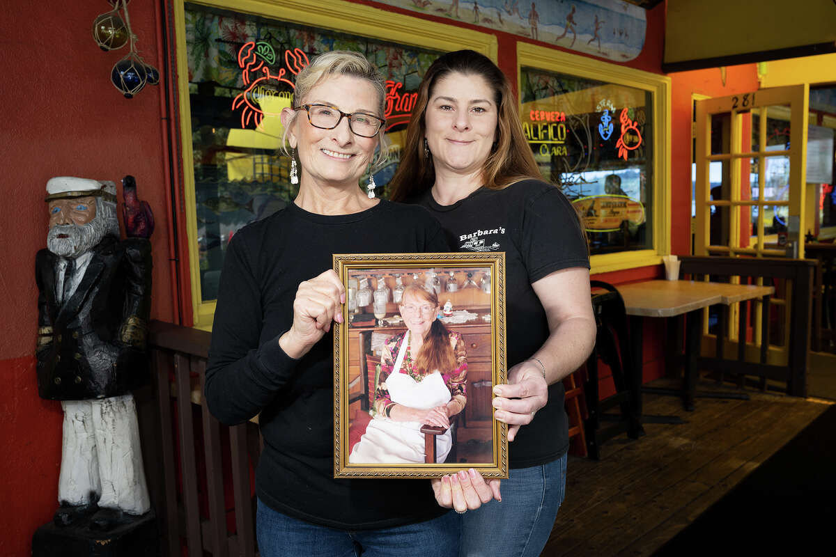 Melodie Madsen and Amanda Howard hold a photo of Barbara Walsh, three generations of owners of Barbaraʻs Fishtrap in Half Moon Bay Calif., May 4, 2023