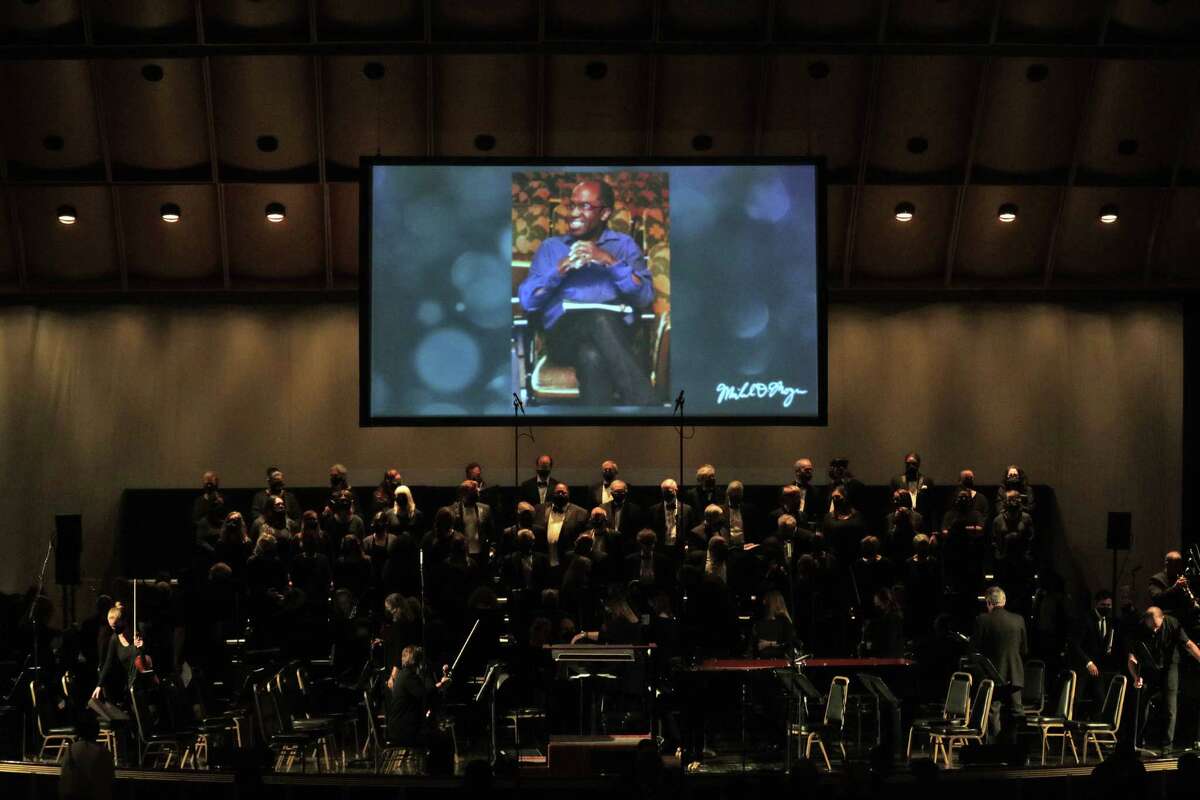 The Oakland Symphony gathers onstage with a photo of Michael Morgan projected above during a memorial event for the longtime music director at the Paramount Theatre in Oakland on Oct. 19, 2021.