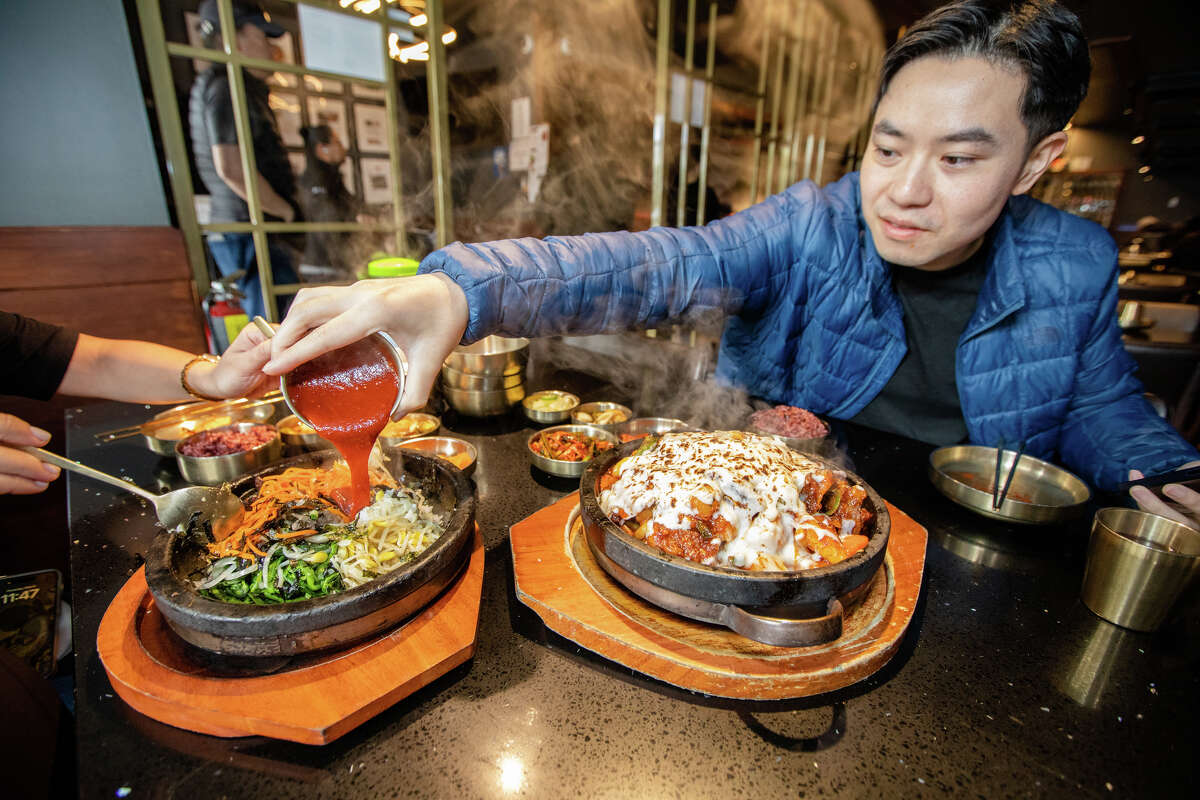 Tim Cheung of Bay Area Foodies pours some gochujang on a dish of bibimbap at Daeho Kalbijjim & Beef Soup in San Francisco on May 9, 2023. He is a social media influencer with hundreds of thousands of followers on Instagram and TikTok.