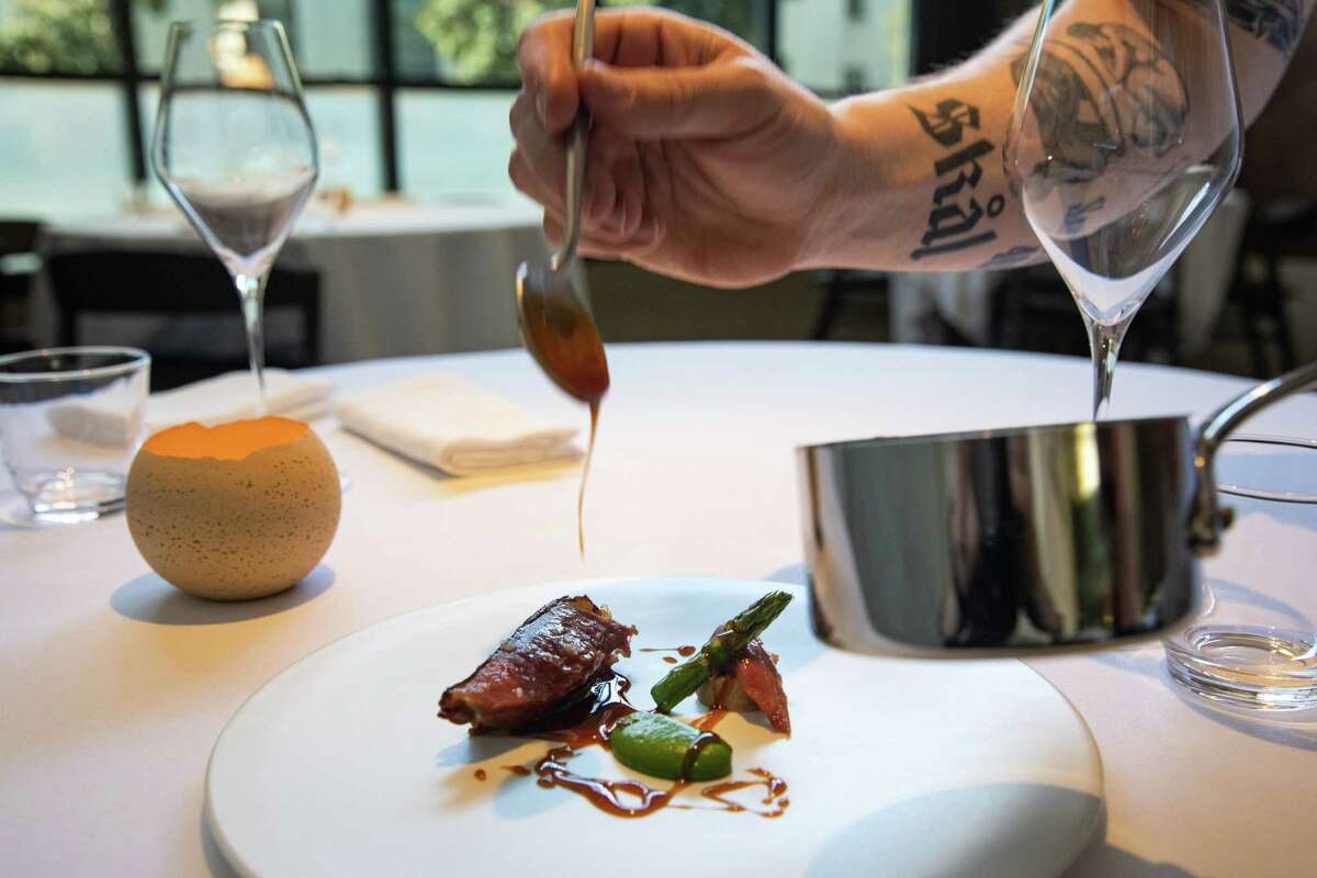 在他的新餐厅窑里，厨师约翰·韦斯利在一盘莫德斯托乳鸽配芦笋和肝甘纳许上勺上烧焦的蜂蜜酱。
