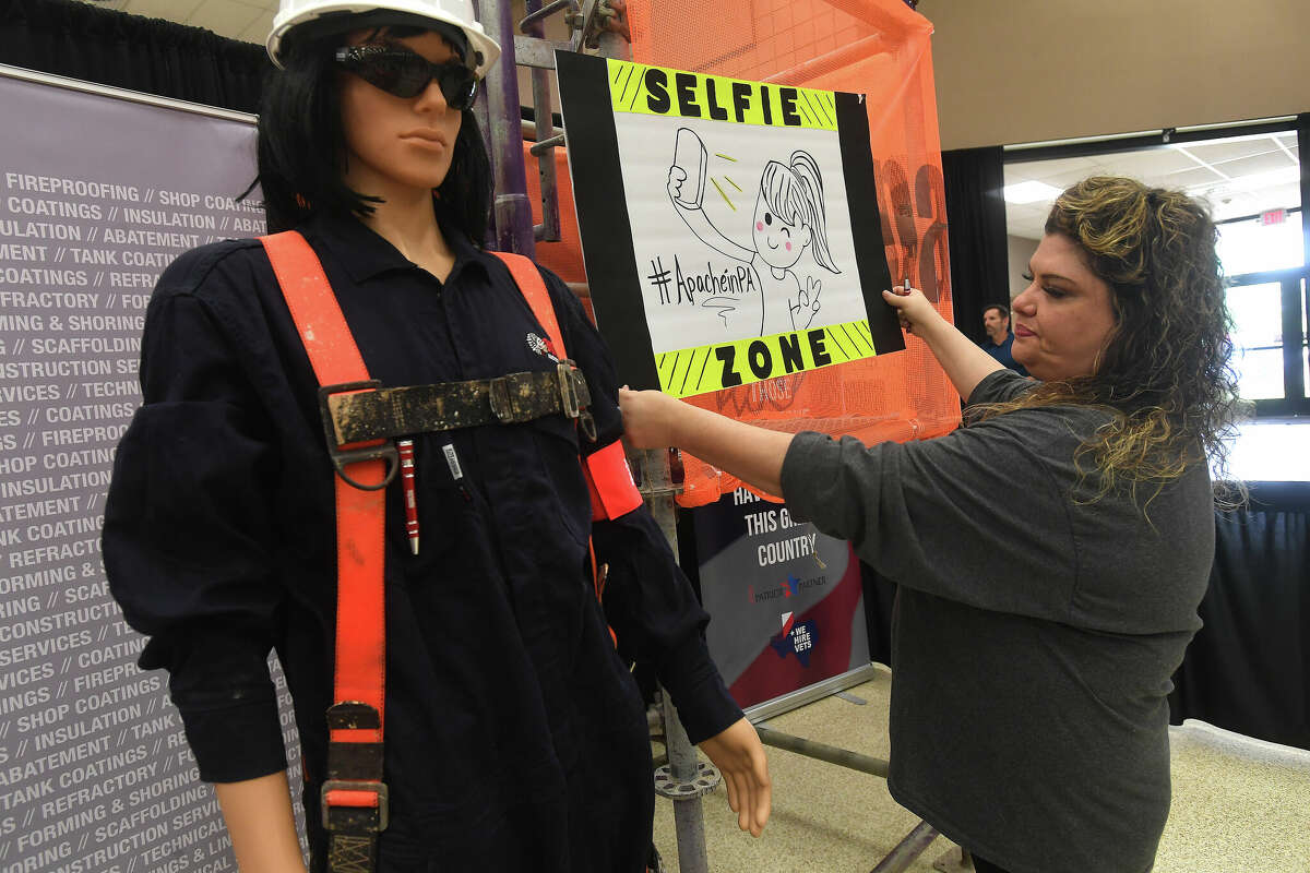 Natalie Presley hangs a sign in Apache Industrial's "selfie zone" at the Spring Job Fair hosted by Workforce Solutions at the Bob A. Bowers Civic Center in Port Arthur. Photo made Thursday, May 11, 2023 Kim Brent/Beaumont Enterprise