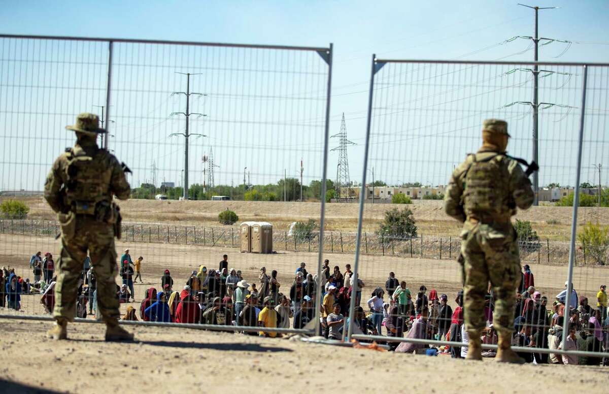 FILE - Migrants wait in line adjacent to the border fence under the watch of the Texas National Guard to enter into El Paso, Texas, Wednesday, May 10, 2023. U.S. authorities say an 8-year-old girl died Wednesday, May 17, in Border Patrol custody, a rare occurrence that comes as the agency struggles with overcrowding. The Border Patrol had 28,717 people in custody on May 10, the day before pandemic-related asylum restrictions expired, which was double from two weeks earlier, according to a court filing.