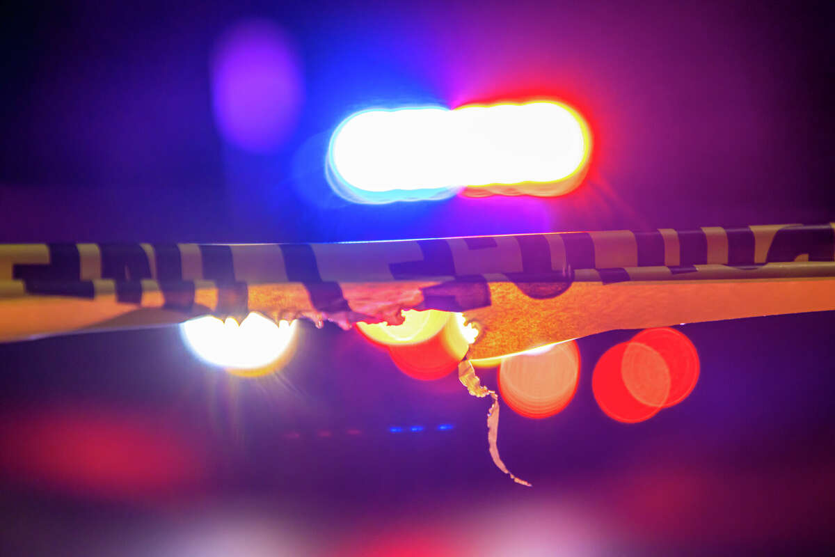 A defocused police car sits behind crime scene tape with flashing lights at night.