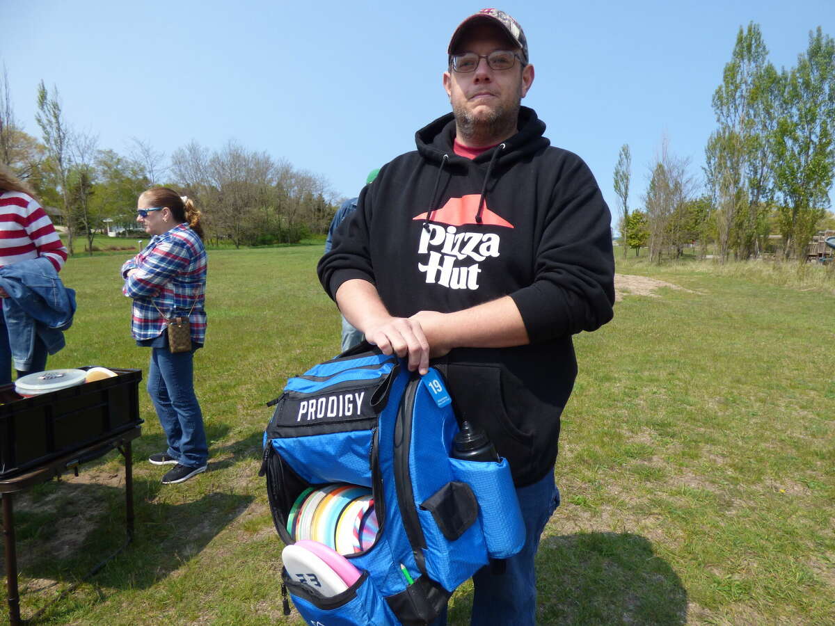 Daniel Campbell holds up his disc golf bag which bears a tag indicating his membership in the Manistee Disc Golf Club.