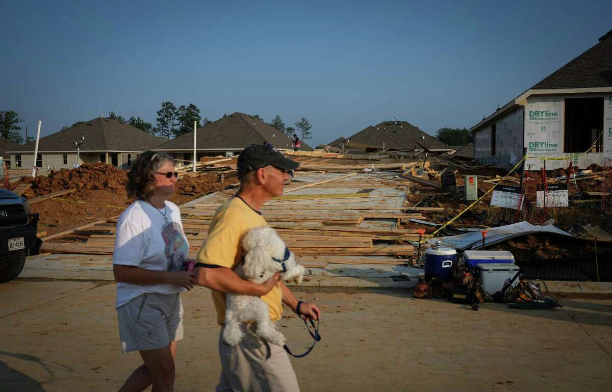 A couple walks by a scene where a house under construction collapsed in high winds Tuesday, May 23, 2023, in Conroe. Officials reported that two people were killed and seven were injured.