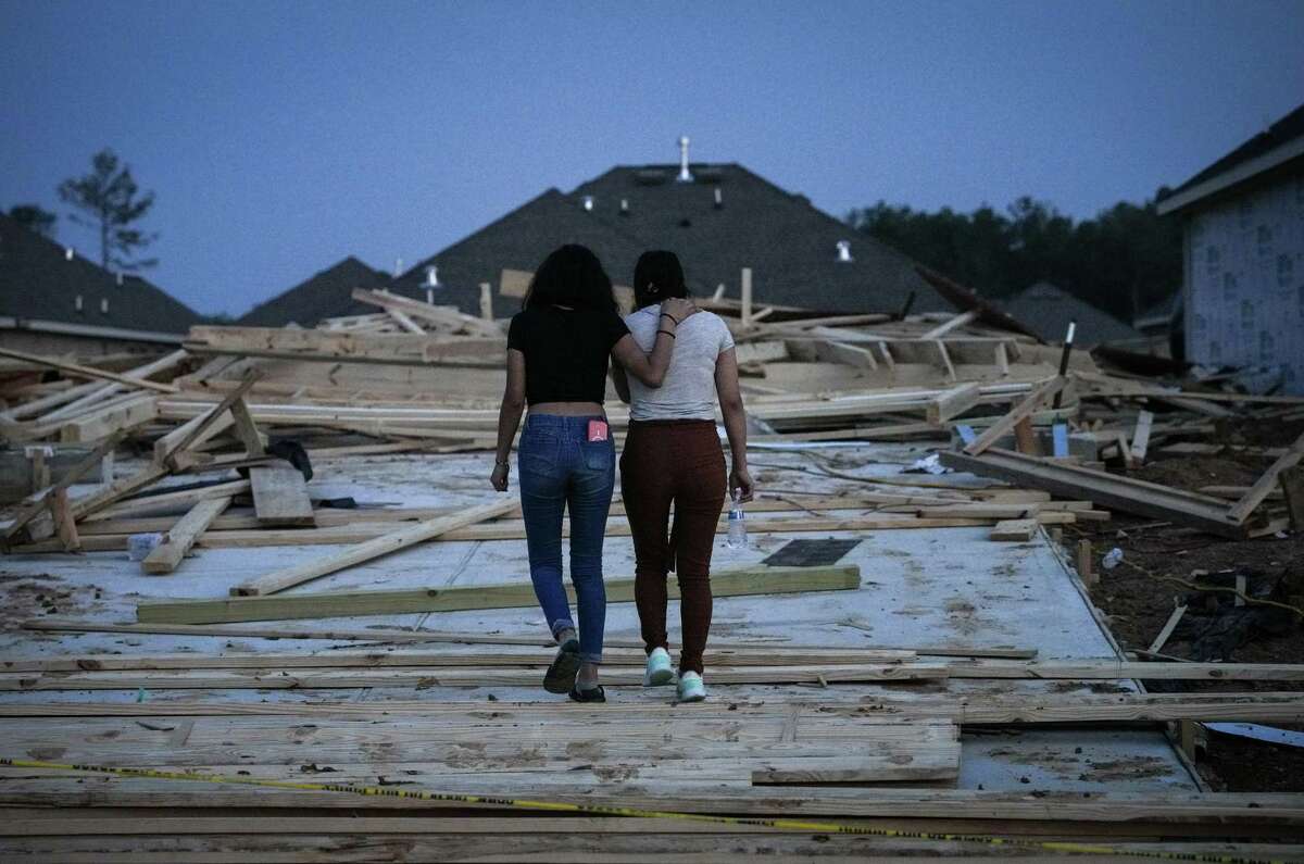 Two women walk into a scene where a house under construction collapsed in strong winds Tuesday, May 23, 2023, in Conroe. Officials said two people were killed and seven were injured. The woman on the right was described as the girlfriend of a man who was killed.