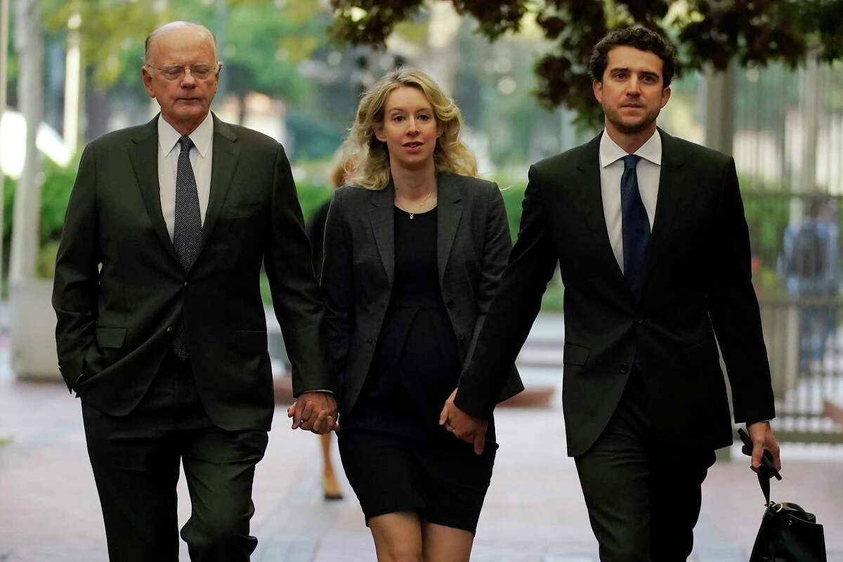 File - Former Theranos CEO Elizabeth Holmes, center, arrives at federal court with her father, Christian Holmes IV, left, and partner, Billy Evans, in San Jose, Calif., Monday, Oct. 17, 2022. As Elizabeth Holmes prepares to report to prison next week, the criminal case that laid bare the blood-testing scam at the heart of her Theranos startup is entering its final phase.